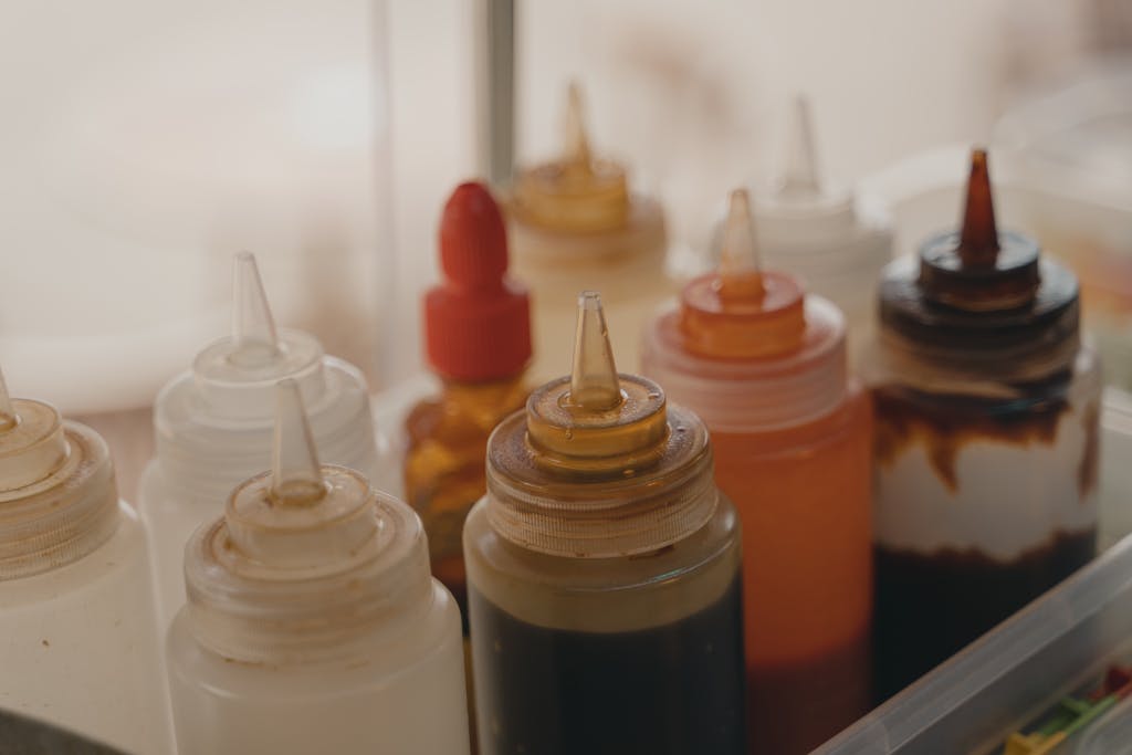Close-up of various condiment squeeze bottles in a food preparation setting.